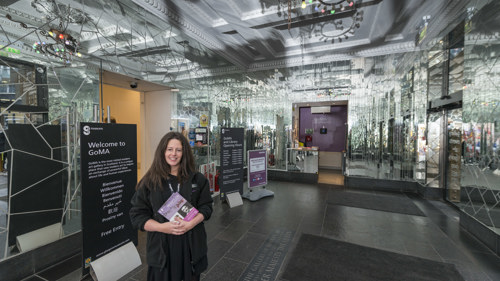 Photograph shows a gallery assistant welcoming visitors to GoMA in the entrance lobby.