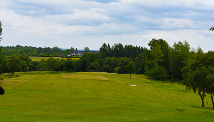view of golf course with putting green surrounded by trees  