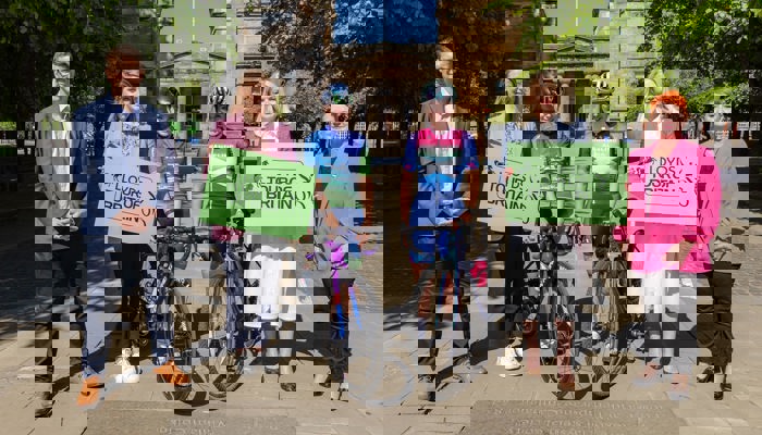 Two professional female cyclists stand in between representatives of the organisers of the Lloyds Tour of Britain Women 2025