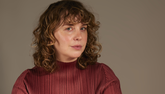 A woman with shoulder-length hair is wearing a red top and looking at the camera