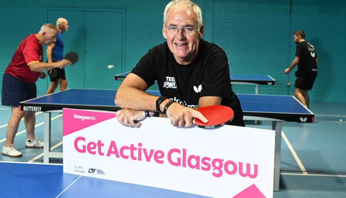 A man holds a red table tennis bat and a sign reading 'Get Active Glasgow'