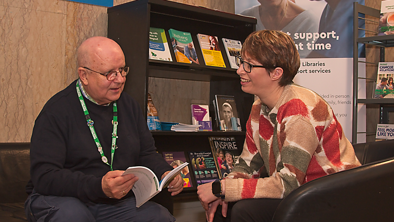 Two people sitting looking at each other smiling with leaflet in hand