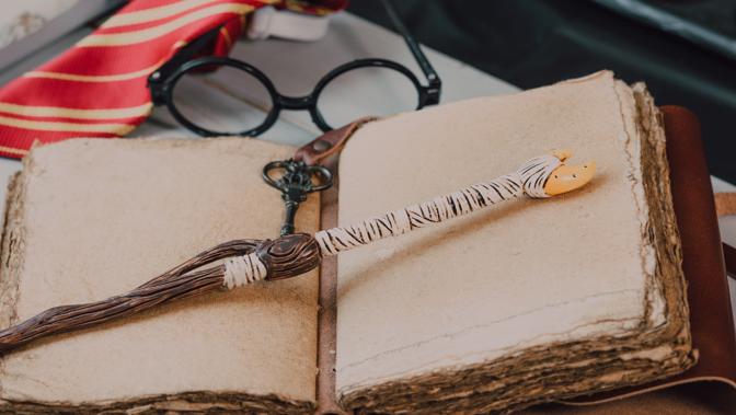Open vintage book, wand, round glasses, key, and a red and yellow striped tie.